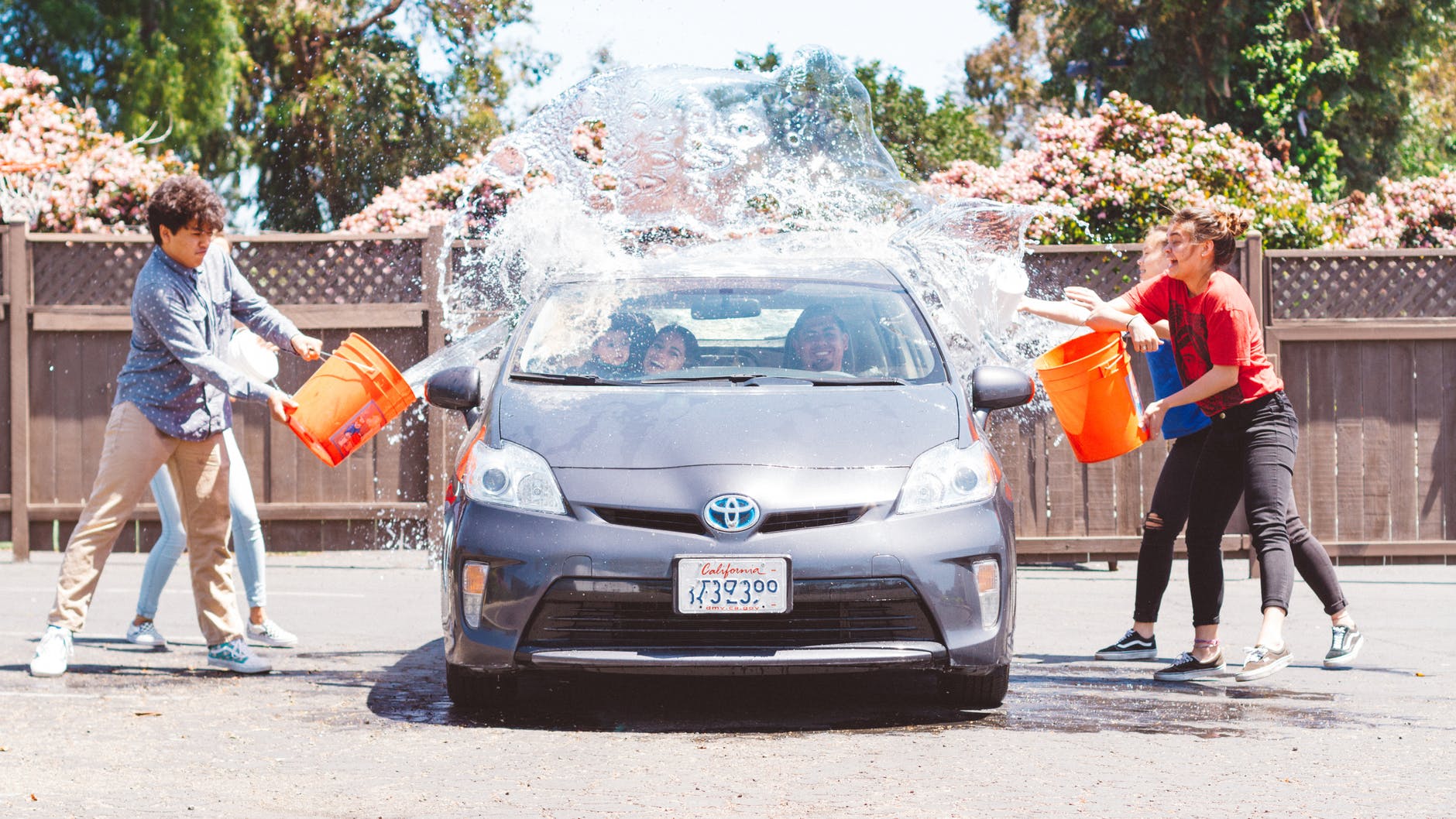 People splashing water from buckets onto a gray car; a fun, outdoor setting.