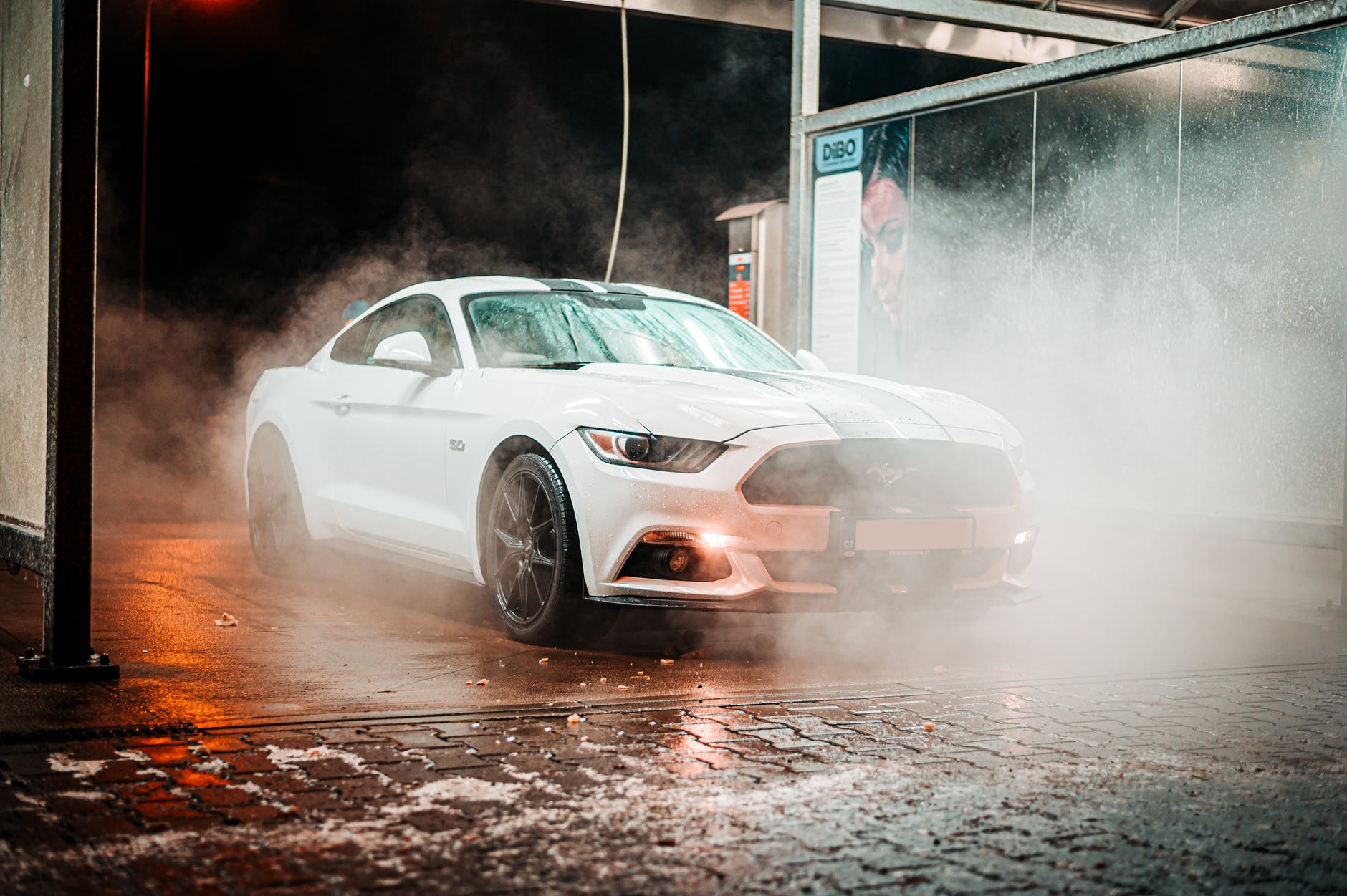 White Ford Mustang being washed at a car wash, water and mist surrounding the car.